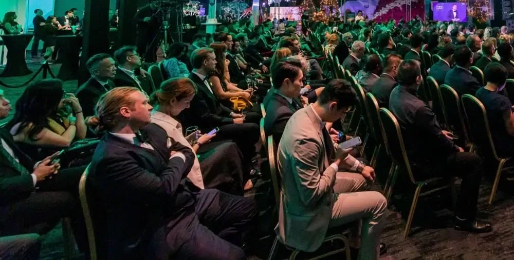 A full conference audience seated in rows under green light