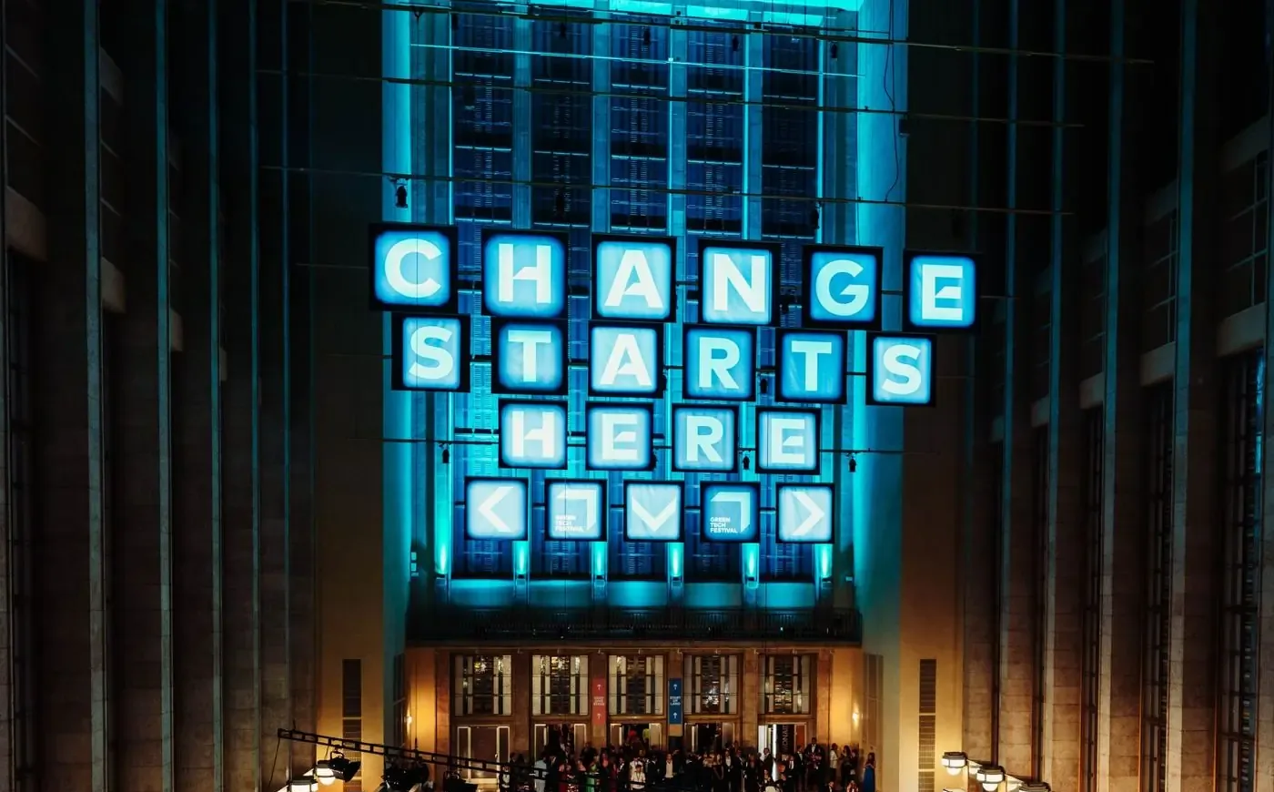 Illuminated lettering reading Change starts here on the facade of the festival venue at night